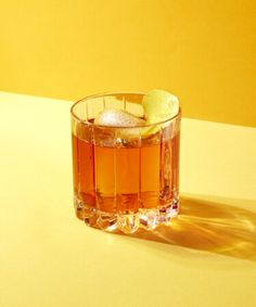 a glass filled with liquid and ice on top of a yellow tablecloth next to an orange wall