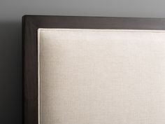 an upholstered bed frame with white linen on the bottom and brown trim around the headboard