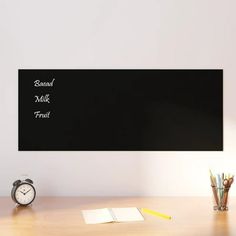 a desk with an alarm clock, pen and pencils on it next to a blackboard