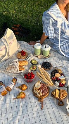 a woman is sitting on the grass with her picnic food spread out in front of her