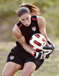 a woman holding a soccer ball in her right hand and wearing gloves on the other side