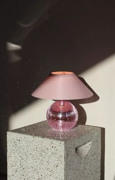 a pink table lamp sitting on top of a block of cement next to a wall