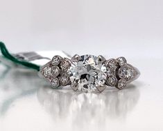 a diamond engagement ring sitting on top of a white surface with a green string attached to it