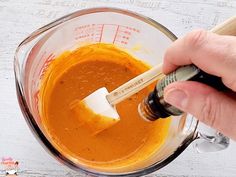 a hand holding a brush in a blender filled with orange liquid and other ingredients