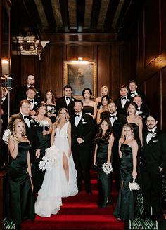 a large group of people in formal wear posing for a photo on the red carpeted stairs