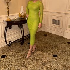 a woman in a green dress standing next to a table with a vase on it