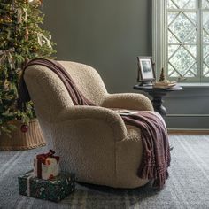 a chair with a blanket on it next to a christmas tree in a living room