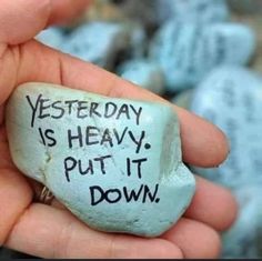 a hand holding a rock with writing on it that says, yesterday is heavy put it down