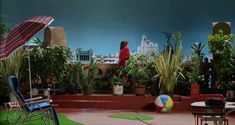 a woman standing on top of a roof next to potted plants and lawn chairs