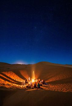 a group of people sitting around a campfire in the middle of desert at night