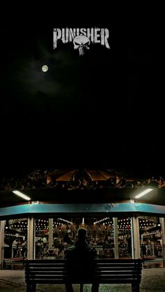 a person sitting on a bench in front of a building at night with the moon above