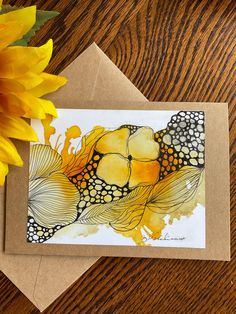 a yellow flower and some brown paper on a wooden table next to a greeting card