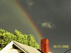 a rainbow in the sky over a white house with brick chimneys and trees behind it