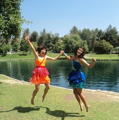 two women jumping in the air with their arms up and legs spread out, near a body of water