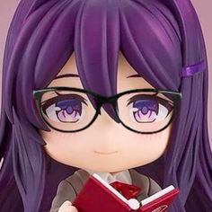 a doll with purple hair and glasses is holding a book in her hand while looking at the camera