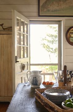 a wooden table topped with plates and bowls next to a window filled with sunlight coming in