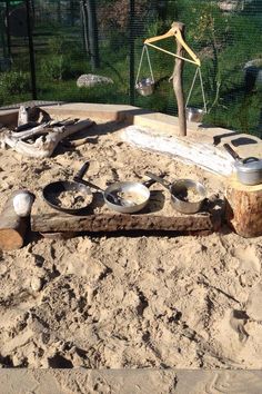 an empty sand pit with bowls and scales on it, in the middle of a park