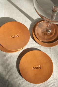 three brown coasters with the word sanita written on one side and an empty wine glass in the other