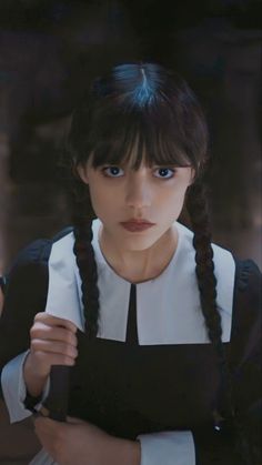 a woman with braids holding a knife and looking at the camera while wearing a black and white dress