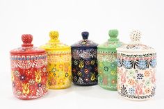 four colorful canisters are lined up on a white surface, one is decorated with flowers and the other has a polka dot design