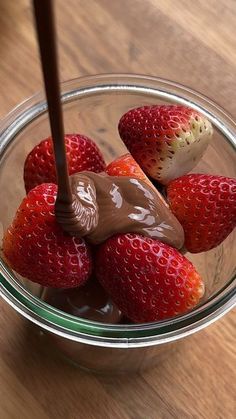 a glass bowl filled with chocolate and strawberries on top of a wooden table next to a spoon