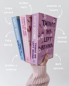 a person's hand holding three books in front of their face with the words things we left behind above them