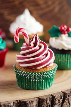 three cupcakes decorated with candy canes on top of a wooden table in front of other cupcakes