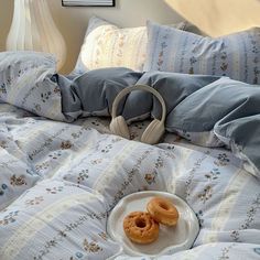 two donuts are sitting on a plate on a bed with headphones in the foreground