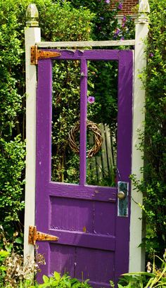 an old purple door with a wreath on it in front of some bushes and trees