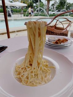 a white plate topped with pasta and sauce on top of a table next to a pool