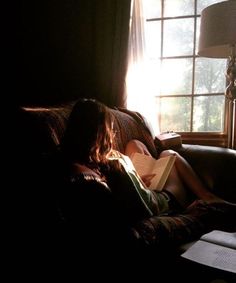 a person sitting on a couch with a book in their lap and sunlight coming through the window