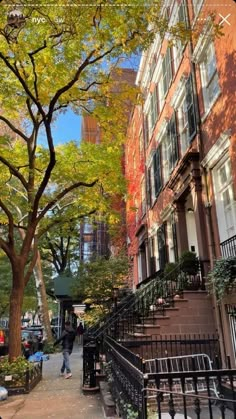 people are walking down the sidewalk in front of tall buildings and trees with leaves on them