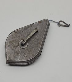 an old metal object on a white surface with a hook in the middle that is attached to it