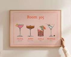 a person holding up a framed poster with different cocktails on it's side