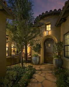 the entrance to a home at night with lights on and plants in pots next to it