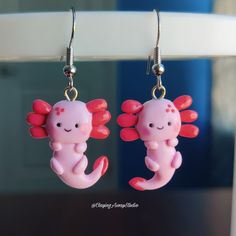 two pink earrings with red and white designs hanging from hooks in front of a mirror