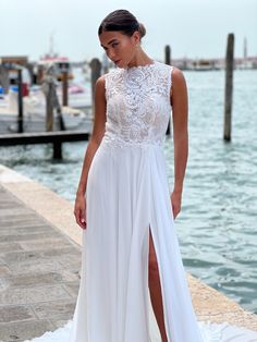 a woman in a white dress standing on a pier next to the water with her leg up