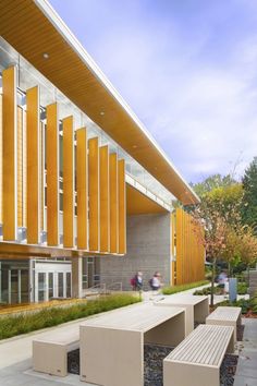 the outside of a building with benches in front of it and people walking on the sidewalk