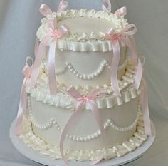 a three tiered wedding cake with pink bows and pearls on the top, sitting on a white platter