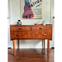 a wooden dresser sitting in the corner of a room next to a painting on the wall