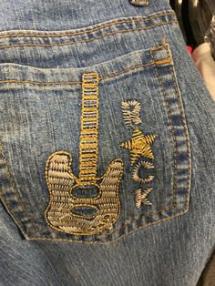 the back of someone's jeans with an embroidered guitar on one side and gold trimmings on the other