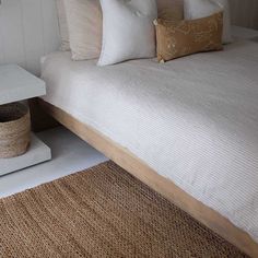 a bed with white sheets and pillows on top of it next to a brown rug