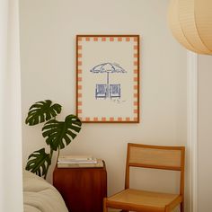 a chair and table in a room with a painting on the wall above it, next to a plant