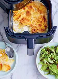 a meal being prepared in an air fryer on a marble counter top next to plates with salad