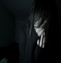 a woman with her hand on her face in the dark, holding her head to her chest