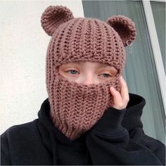 a woman wearing a knitted bear mask with ears on her head, covering her face