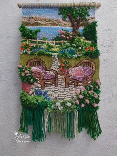 a tapestry hanging on the side of a wall with two chairs and flowers in it