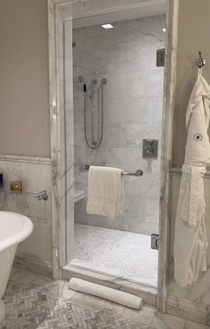 a bathroom with marble walls and flooring has a glass shower door that is open