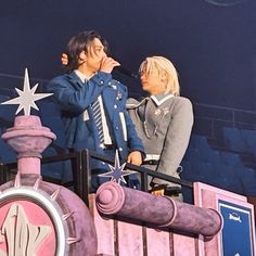 two people standing next to each other on top of a train at an amusement park