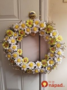 a wreath with yellow and white flowers hanging on a door